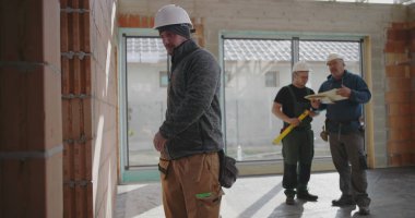 Duvarı kalemle ölçen inşaat işçisi, güvenlik miğferinde odaklanmış miğferle içeride tuğla yapı, hassasiyet ve detaylara dikkat ediyor.