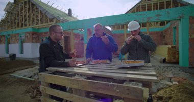 İnşaat işçileri öğle yemeği molasında pizza kutularıyla derme çatma masa, rahat atmosfer, etkin inşaat alanında açık hava yemeği, kaynaşma ve takım çalışması.