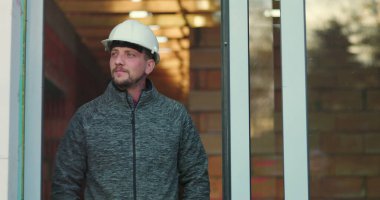 Şapkalı genç bir inşaat işçisi, kapının önünde duruyor, kendine güveniyor, inşaat projesine kendini adamış, inşaat alanında deneyimli ve odaklanmış.