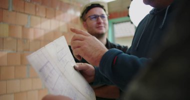 İnşaat planlarını, miğferleri, takım çalışmasını ve işbirliğini tartışan inşaat işçilerinin ayrıntılı görüşü, plan üzerinde yoğunlaşmak, inşaat alanı