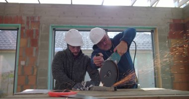 Metal üzerinde elektrikli öğütücü kullanan inşaat işçileri kıvılcımlar üretiyor, iş başında takım çalışması yapıyor, güvenlik kaskı ve koruma için gözlük takıyor, yenileme sahasını yeniliyor.
