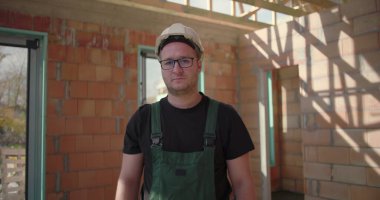 İnşaat işçilerinin baret ve gözlükleriyle yakın çekimleri bitmemiş bir binanın içinde duruyor, ciddi ve adanmış görünüyor, hassasiyeti temsil ediyor ve işe odaklanıyor.