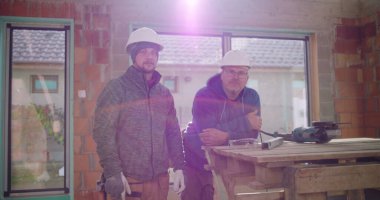 Kısmen inşa edilmiş yapının yanında duran iki inşaat işçisi, güvenlik kaskı takıyorlar, inşaat sahasında takım çalışması, inşaat endüstrisi, gündüz ayarı