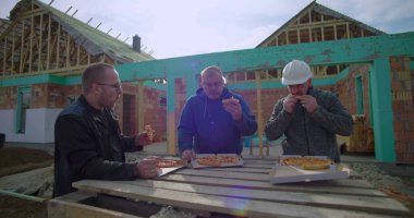 İnşaat işçileri öğle yemeği molasında pizza kutularıyla derme çatma masa, rahat atmosfer, etkin inşaat alanında açık hava yemeği, kaynaşma ve takım çalışması.