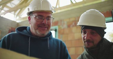 İnşaat alanındaki planları inceleyen inşaat işçilerinin yakın çekimleri, proje planlama ve işbirliği, güvenlik kaskları ve takım çalışması üzerine odaklandı.