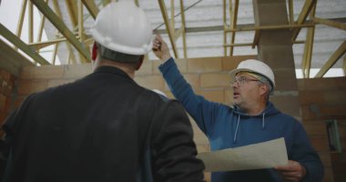 İnşaat ekibi, bitmemiş bir binanın içindeki planları gözden geçirir, inşaat projesinin tasarımını koordine eder ve mimari ayrıntıları tartışır.