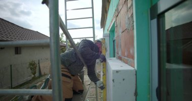 İnşaat sırasında dış duvar yalıtımının ölçülmesi ve seviyelendirilmesi, ev inşaatının enerji tasarrufu için hassas hizalanmasını sağlayan sert şapkalı odaklı müteahhit