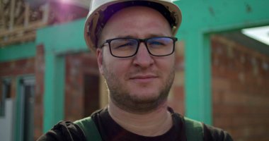 İnşaat alanında kendine güveni olan, inşaat projesine adanmış, sanayi ve işçilikle gurur duyan kasklı bir erkek inşaat işçisi.