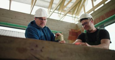 İnşaat işçileri inşaat sahasında odun testeresi, inşaat iskeletinde takım çalışması, bir işçi keserken diğeri yardım ediyor, hassasiyet ve güvenliğe odaklanıyor