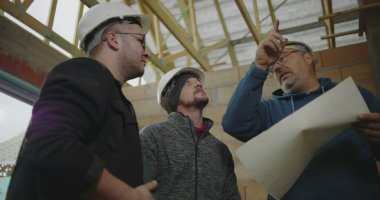 İnşaat halindeki bir binanın planlarını tartışan üç inşaat işçisi, mimari ayrıntılar ve proje planlamasına odaklandı