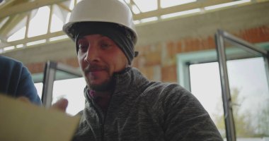 İnşaat alanındaki inşaat işçilerinin inşaat halindeki bir binanın içindeki mimari planlara odaklandığı yakın plan.