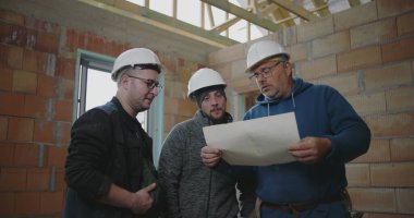İnşaat ekibi, bitmemiş bir binanın içindeki planları gözden geçirir, inşaat projesinin tasarımını koordine eder ve mimari ayrıntıları tartışır.