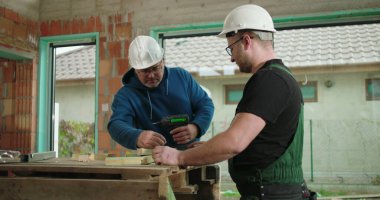 Ahşap parçası üzerinde çalışan iki adam, inşaat alanında odaklanmış takım çalışması, koruyucu kasklar takan, yapı iskeleti montajlayan, bina yapısında takım çalışması yapan