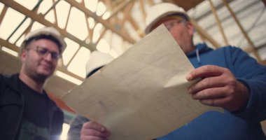 İnşaat işçisi ayrıntılı planlara işaret ediyor, bitmemiş bir bina yapısında mimari planlar ve proje koordinasyonu üzerinde işbirliği yapıyor