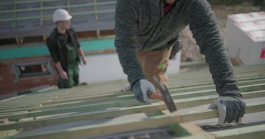 İşçi çatıdaki çivileri güvence altına almak için çekiç kullanıyor, eldiven ve kask takıyor, inşaat alanındaki el ve aletlere yakından bakıyor, proje çalışmalarının bir parçası.