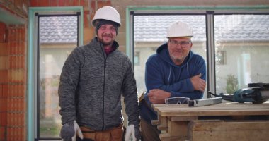 İnşaat alanındaki çalışma tezgahında gülümseyen iki inşaat işçisi, inşaat alanındaki takım çalışması ve güvenlik, kendinden emin ve işbirlikçi atmosfer