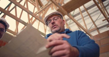 İnşaat işçisi ayrıntılı planlara işaret ediyor, bitmemiş bir bina yapısında mimari planlar ve proje koordinasyonu üzerinde işbirliği yapıyor