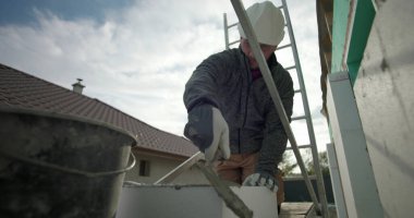 Havan topunu malayla hazırlamak, miğferli inşaat işçisi ve yapı iskelesinde eldiven, konut yenileme, duvarcılık malzemelerinin yakın çekim kullanımı