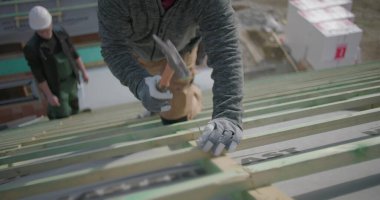 İşçi çatıdaki çivileri güvence altına almak için çekiç kullanıyor, eldiven ve kask takıyor, inşaat alanındaki el ve aletlere yakından bakıyor, proje çalışmalarının bir parçası.