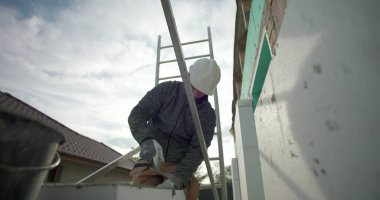 Havan topunu malayla hazırlamak, miğferli inşaat işçisi ve yapı iskelesinde eldiven, konut yenileme, duvarcılık malzemelerinin yakın çekim kullanımı