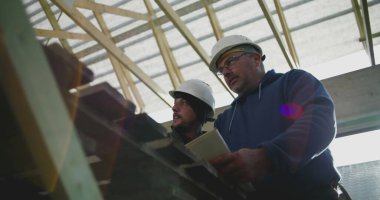 Yapısal çerçeve ve yapı planlarını gözden geçiren inşaat işçileri, yenileme projesinde takım çalışması, ayrıntıları tartışan, sahada güvenlik kaskı takan