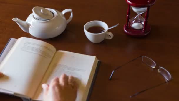 Руки Жінки Залишаються Через Книгу Розміщену Столі Біля Чашки Чаю — стокове відео