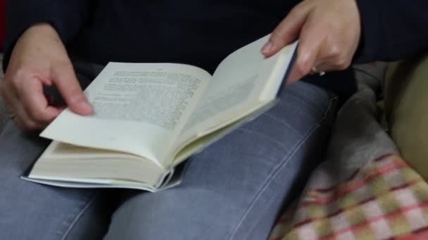 一个女人舒服地坐在沙发上翻阅一本书 — 图库视频影像