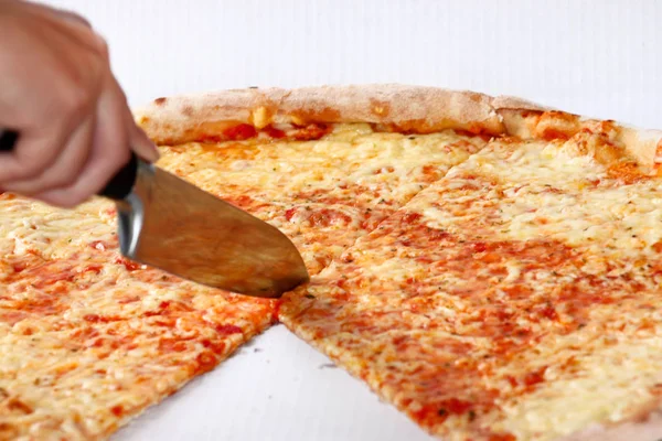 Woman\'s hand with a knife cut the pizza. Delicious pizza Margarita. Take out freshly baked italian pizza being held in a box, close up. Italian traditional classic pizza Margarita. Fast Food.
