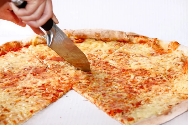 Woman\'s hand with a knife cut the pizza. Delicious pizza Margarita. Take out freshly baked italian pizza being held in a box, close up. Italian traditional classic pizza Margarita. Fast Food.