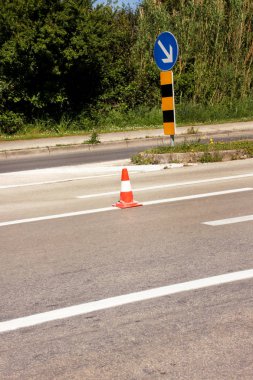 Yolda çalış. Trafik işaretli inşaat konileri sağdaki tabelayı tutar. Asfalt üzerinde beyaz ve turuncu çizgileri olan trafik konileri. Trafik işaretleri ve yol bakımı, inşaat tabelası altında..