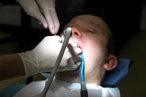 Dental tooth polishing. Teeth cleaning, dental hygiene. Dentist at work in his dentist clinic and office is polishing of patient teeth with tools mirror, soft dental brush and suction tube in mouth.