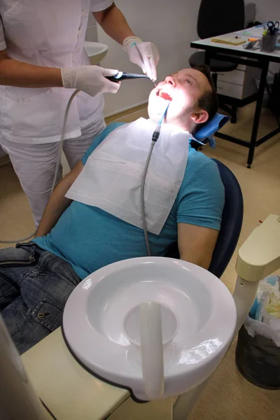 Dental tool for rinsing teeth. Teeth cleaning, dental hygiene. Dentist at work in his dentist clinic and office is rinsing of patient teeth with mirror, cleaning tool spray and suction tube in mouth.