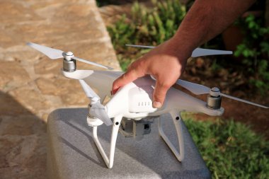 Adam elinde bir dron holding ve yeni teknoloji kullanarak. Beyaz dört helikopter uçak ve fotoğrafçı adam ellerini. Uzaktan kontrol paneli ekran ve kontrolleri ile profesyonel casus uçak pilot tutar.