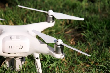 Beyaz quadcopter dron çimenlerin üzerinde 4 k dijital kamera ile fotoğraf çekmek, görüntüleri yukarıdan kayıt için havada uçmak için kalkış için hazır. Dört motorlar, pervaneleri, kamera ve kırmızı uyarı lambaları ile robot.