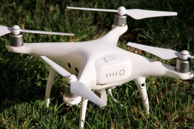 Beyaz quadcopter dron çimenlerin üzerinde 4 k dijital kamera ile fotoğraf çekmek, görüntüleri yukarıdan kayıt için havada uçmak için kalkış için hazır. Dört motorlar, pervaneleri, kamera ve kırmızı uyarı lambaları ile robot.