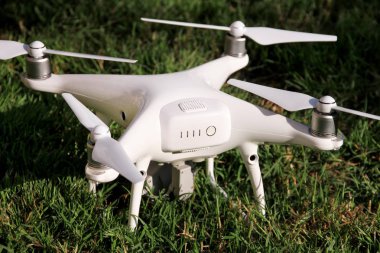 Beyaz quadcopter dron çimenlerin üzerinde 4 k dijital kamera ile fotoğraf çekmek, görüntüleri yukarıdan kayıt için havada uçmak için kalkış için hazır. Dört motorlar, pervaneleri, kamera ve kırmızı uyarı lambaları ile robot.