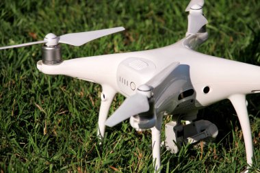 Beyaz quadcopter dron çimenlerin üzerinde 4 k dijital kamera ile fotoğraf çekmek, görüntüleri yukarıdan kayıt için havada uçmak için kalkış için hazır. Dört motorlar, pervaneleri, kamera ve kırmızı uyarı lambaları ile robot.