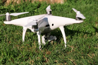 Beyaz quadcopter dron çimenlerin üzerinde 4 k dijital kamera ile fotoğraf çekmek, görüntüleri yukarıdan kayıt için havada uçmak için kalkış için hazır. Dört motorlar, pervaneleri, kamera ve kırmızı uyarı lambaları ile robot.