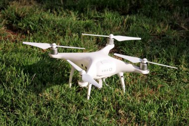 Beyaz quadcopter dron çimenlerin üzerinde 4 k dijital kamera ile fotoğraf çekmek, görüntüleri yukarıdan kayıt için havada uçmak için kalkış için hazır. Dört motorlar, pervaneleri, kamera ve kırmızı uyarı lambaları ile robot.