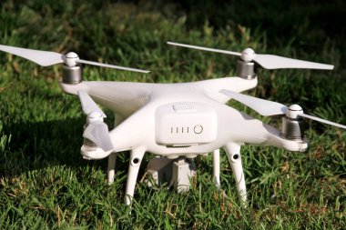 Beyaz quadcopter dron çimenlerin üzerinde 4 k dijital kamera ile fotoğraf çekmek, görüntüleri yukarıdan kayıt için havada uçmak için kalkış için hazır. Dört motorlar, pervaneleri, kamera ve kırmızı uyarı lambaları ile robot.