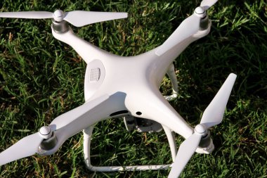 Beyaz quadcopter dron çimenlerin üzerinde 4 k dijital kamera ile fotoğraf çekmek, görüntüleri yukarıdan kayıt için havada uçmak için kalkış için hazır. Dört motorlar, pervaneleri, kamera ve kırmızı uyarı lambaları ile robot.