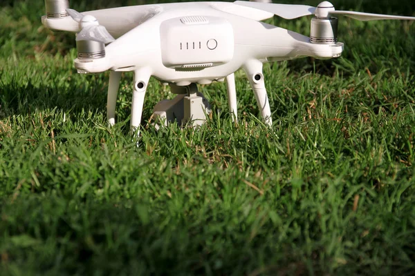 White quadcopter Drone with 4K digital camera on grass is ready for take off to fly in air to take photos, record footage from above. Drone with four motors, propellers, camera and red warning lights.