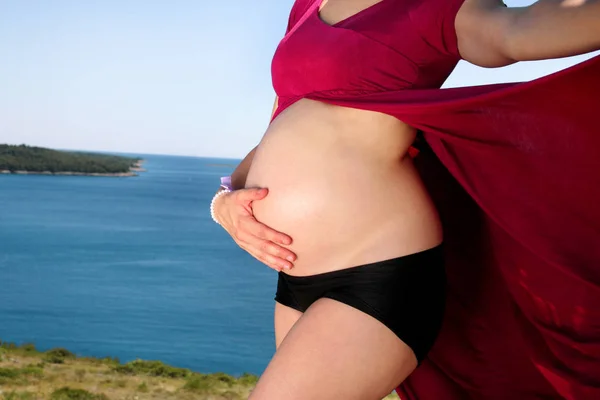 美丽的孕妇和夫人拥抱和抱着她怀孕的肚子 站在自然环境中 等待婴儿 妈妈在海上和天空的自然背景下手 — 图库照片