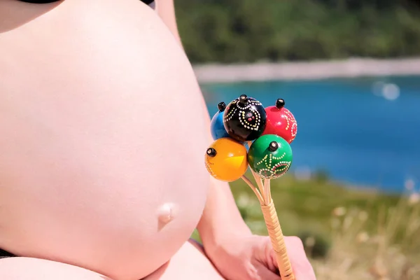 孕妇在怀孕的腹部手持经典的彩色拨浪鼓婴儿钟玩具 未来的妈妈和父母正在等待着宝贝 爱和幸福 出生期望概念 — 图库照片