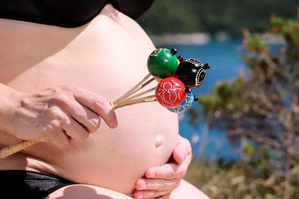 孕妇在怀孕的腹部手持经典的彩色拨浪鼓婴儿钟玩具 未来的妈妈和父母正在等待着宝贝 爱和幸福 出生期望概念 — 图库照片