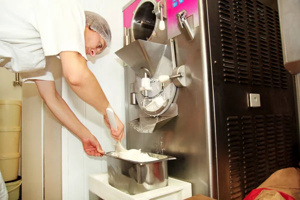 Kadın pudra Ice cream maker makina üzerinde çalışıyor. Vanilya ve beyaz çikolatalı dondurma ve üreten çelik konteyner içine düşüyor. İtalyan kremalı dondurma endüstriyel hazırlanması.