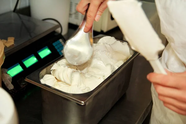 Woman working at ice cream factory is decorations of creamy vanilla and white chocolate ice cream with dice and chunks of chocolate in steel container. Pouring chocolate in tray with frozen ice cream.