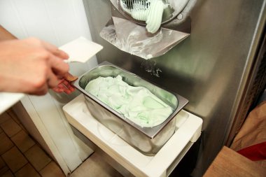 Şef üniforma içinde kadın pudra Ice cream maker makina üzerinde çalışıyor. Nane dondurma lezzeti ve üreten çelik konteyner içine düşüyor. İtalyan kremalı dondurma endüstriyel hazırlanması.