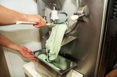 Şef üniforma içinde kadın pudra Ice cream maker makina üzerinde çalışıyor. Nane dondurma lezzeti ve üreten çelik konteyner içine düşüyor. İtalyan kremalı dondurma endüstriyel hazırlanması.