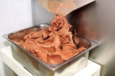 Ice cream making machine produces black chocolate ice cream flavors and it falls into steel container. Industrial preparation of italian creamy ice cream. Producing chocolate ice cream with machine. clipart